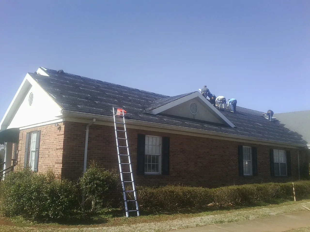 Crew tearing shingles off a brick ranch roof with a ladder set — Metal Roof Repair work by our crew in Fishers Island