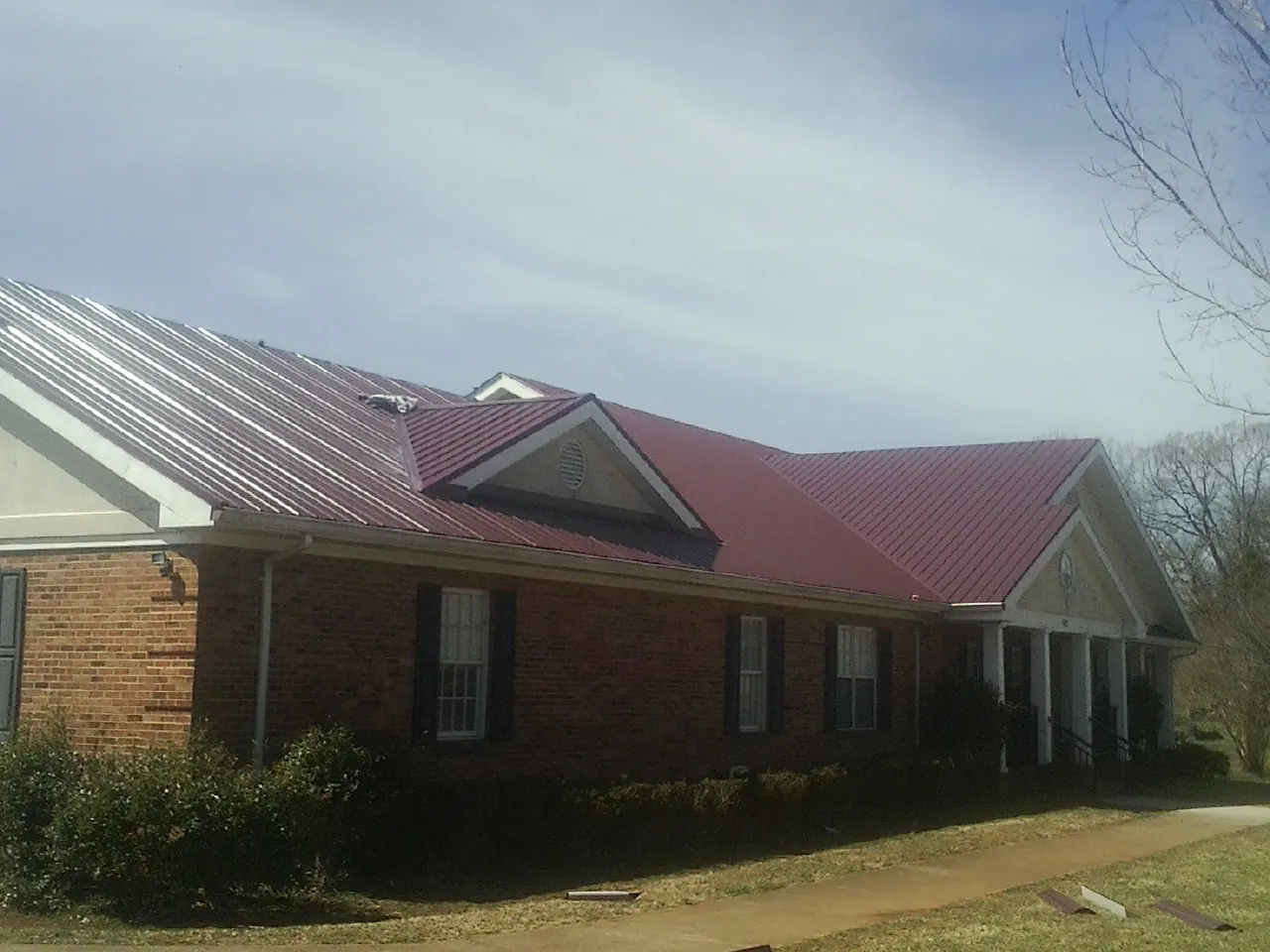 Red metal roof with gabled entries on a long brick building, from a Hail Damage Roof Repair job in Fishers Island