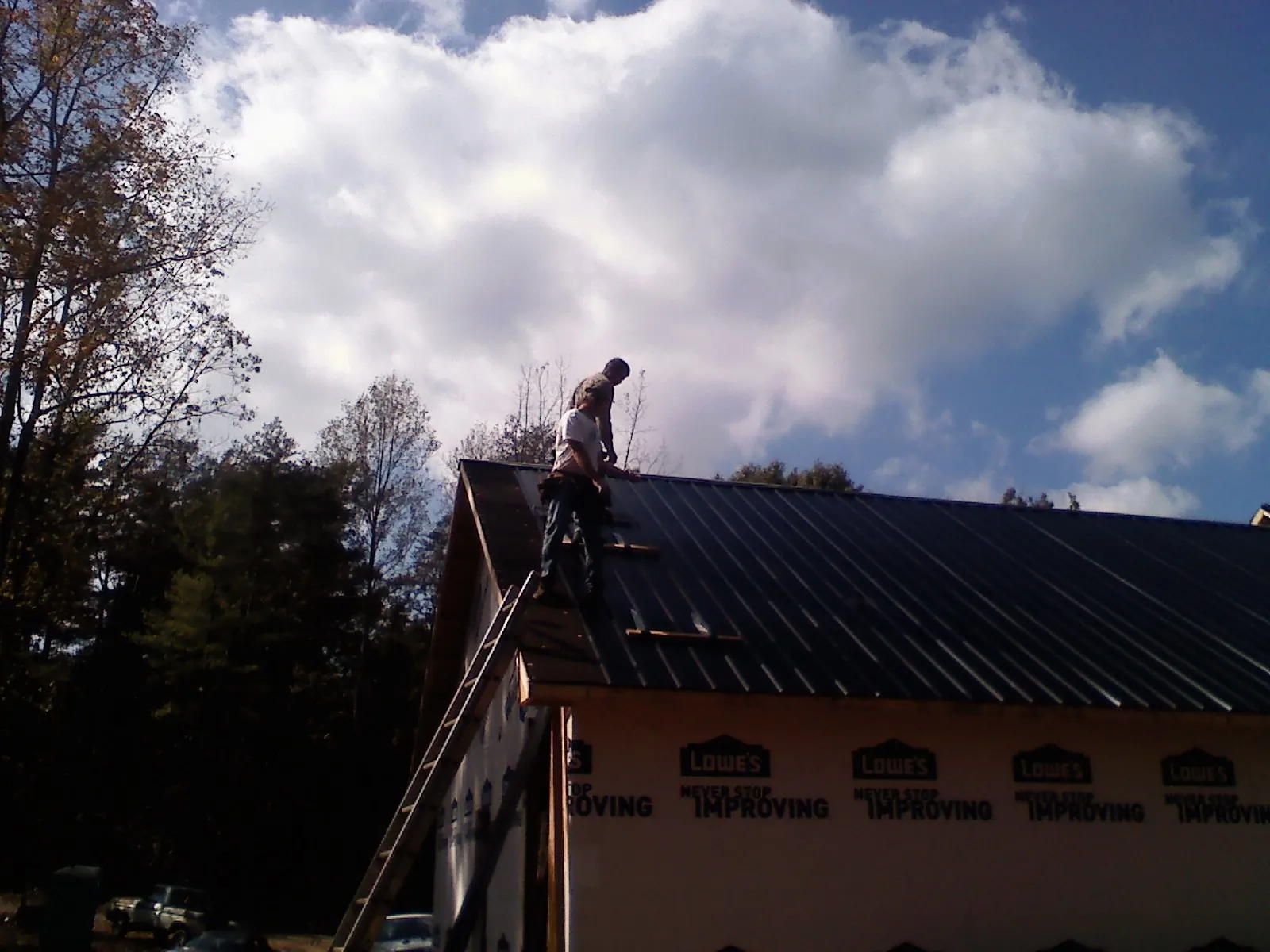 Roofer fastening dark metal panels high against a cloudy sky, from a Roof Inspection job in Fishers Island