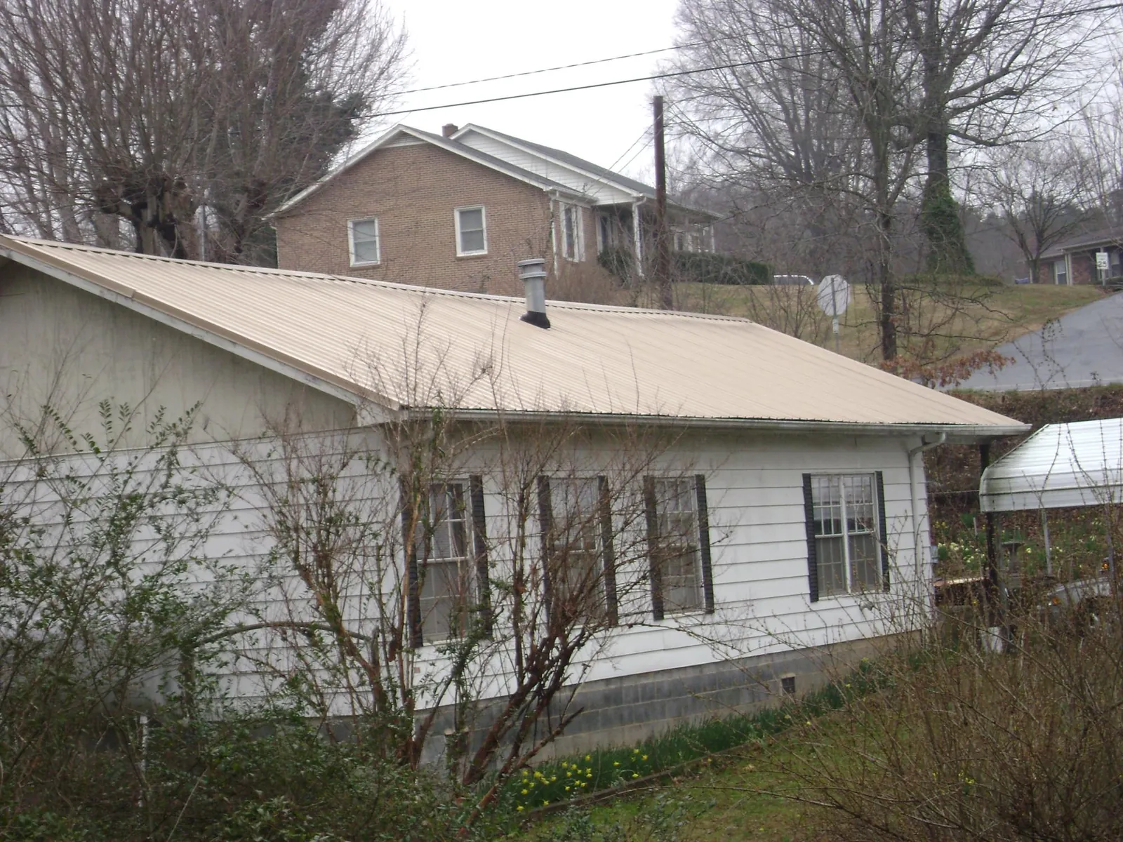 Tan metal roof on a white sided house set into a hillside — Commercial Roofing by Roofing Brothers in Fishers Island